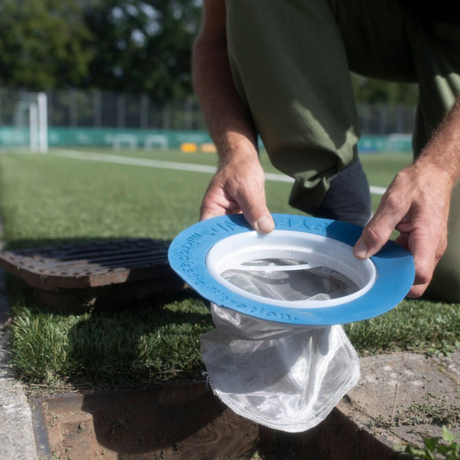 Person die in einen Abfluss auf einem Sportplatz eienn Kunstrasen Filter einsetzt.