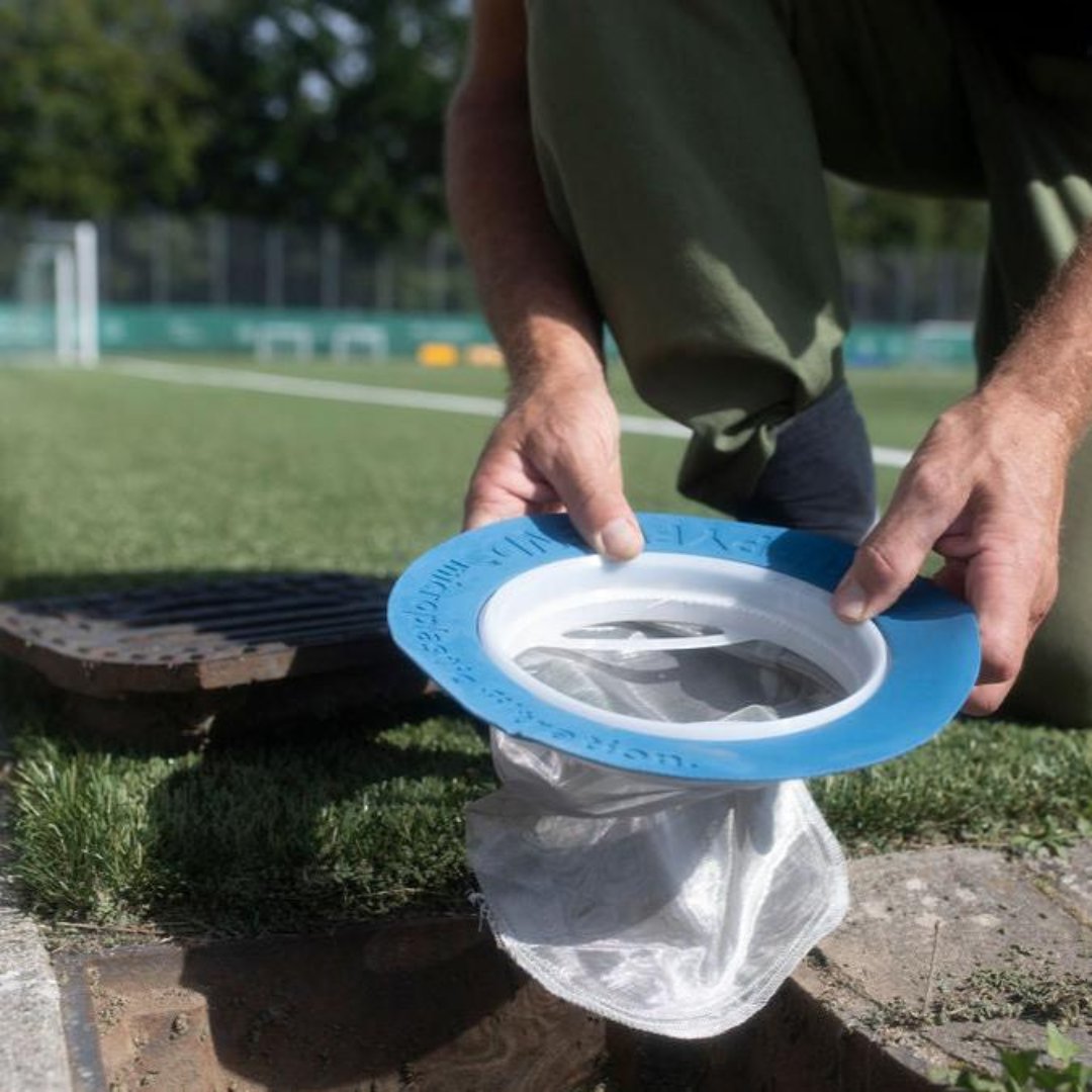 Person die in einen Abfluss auf einem Sportplatz eienn Kunstrasen Filter von Guppyfriend einsetzt.